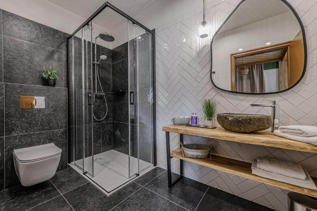 A modern bathroom with a glass-enclosed shower, a wooden vanity, and a herringbone-patterned wall.