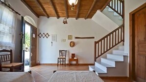 Un dormitorio con cama, una silla de madera, un escritorio, una escalera y una puerta.