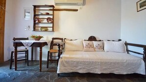 Una habitación acogedora con una cama, una silla de madera, una mesa con una planta, una estantería con adornos y un equipo de aire acondicionado.