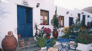 Un edificio blanco con puerta azul, plantas en macetas y mesas al aire libre.