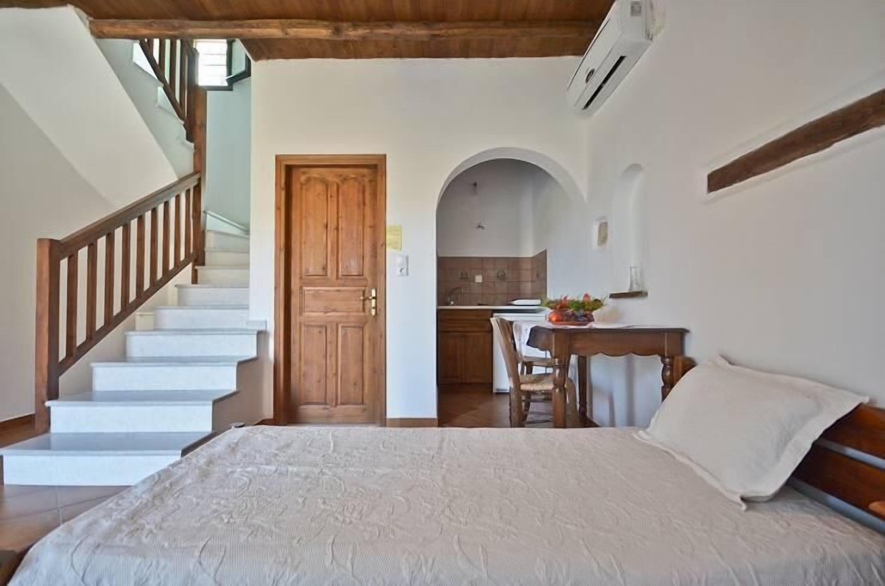 A bedroom with a bed, a wooden staircase, a kitchen area, and an arched doorway.
