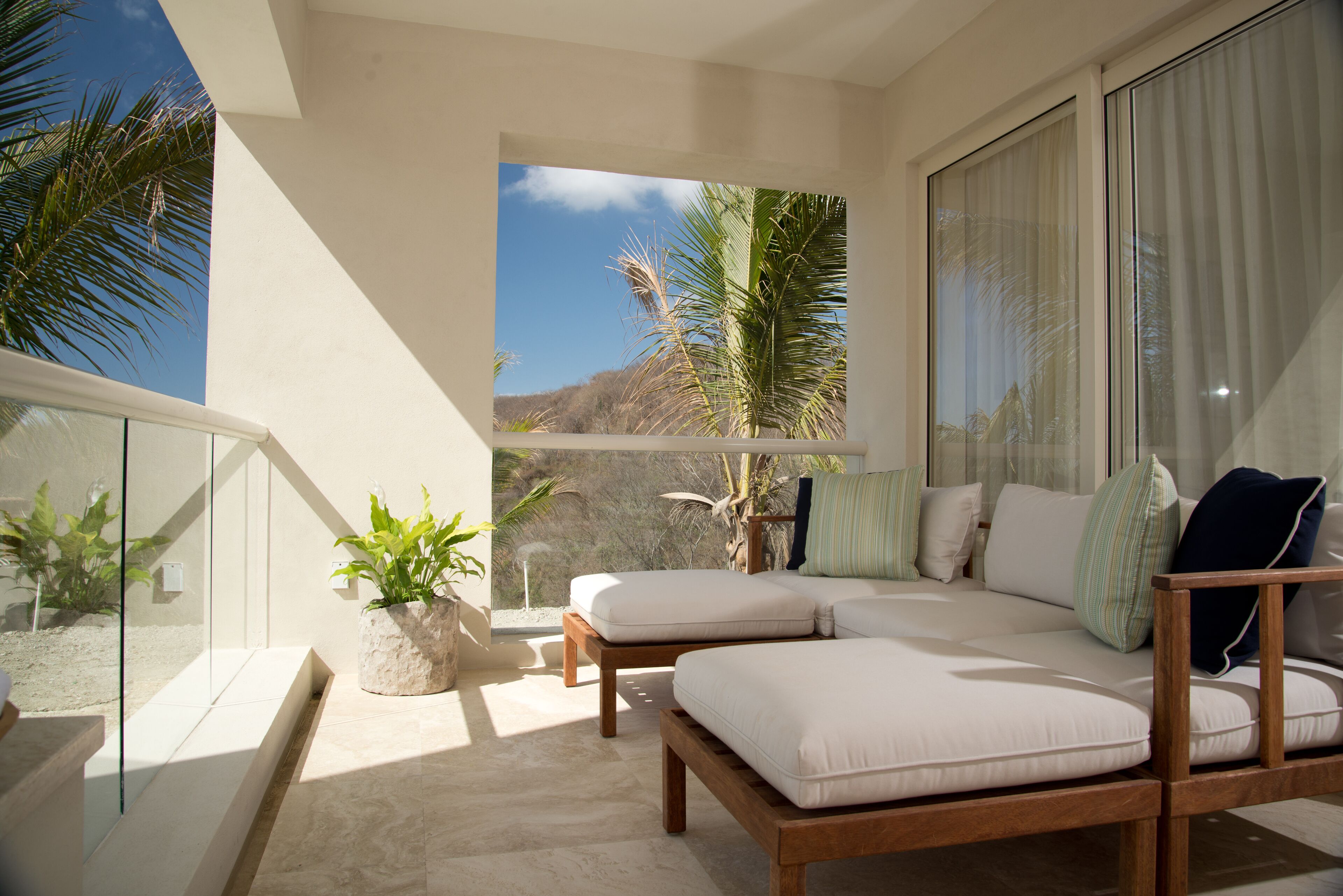 A balcony with a sofa, a potted plant, and a view of palm trees and a mountain.