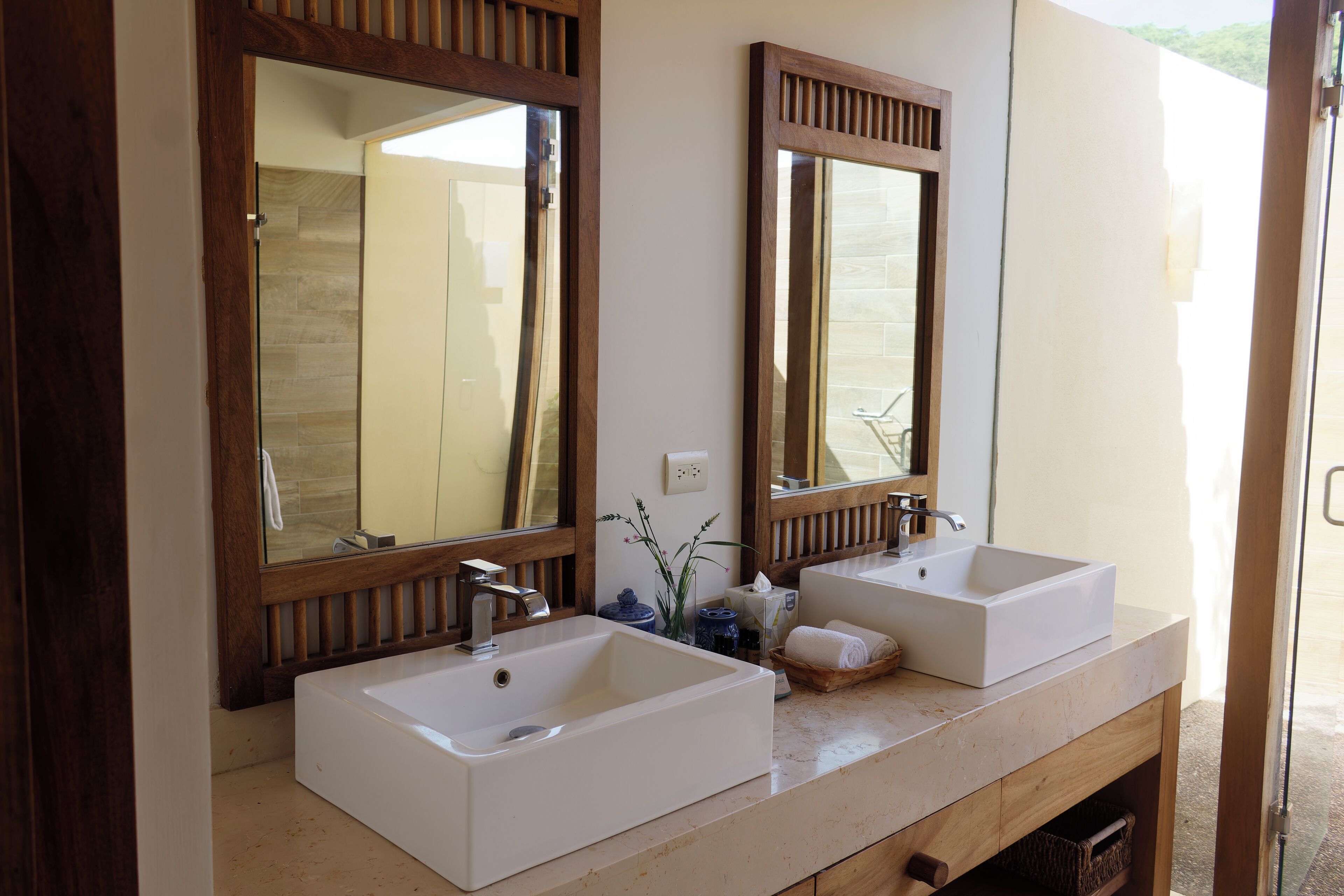 Un bagno con due lavabi bianchi, specchi con cornice in legno e un piano d'appoggio color beige.