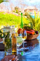 Una mesa con una jarrón, una botella, un vaso y un cuenco de fruta.