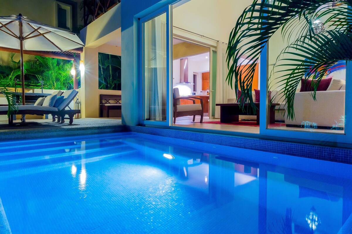 Una piscina interior con agua cristalina y azul, rodeada de sillones de descanso y sombrillas.