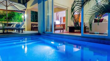 Una piscina interior con agua cristalina y azul, rodeada de sillones de descanso y sombrillas.
