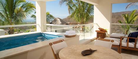 A poolside area with a table and chairs, a thatched-roof structure, and a view of palm trees and mountains.