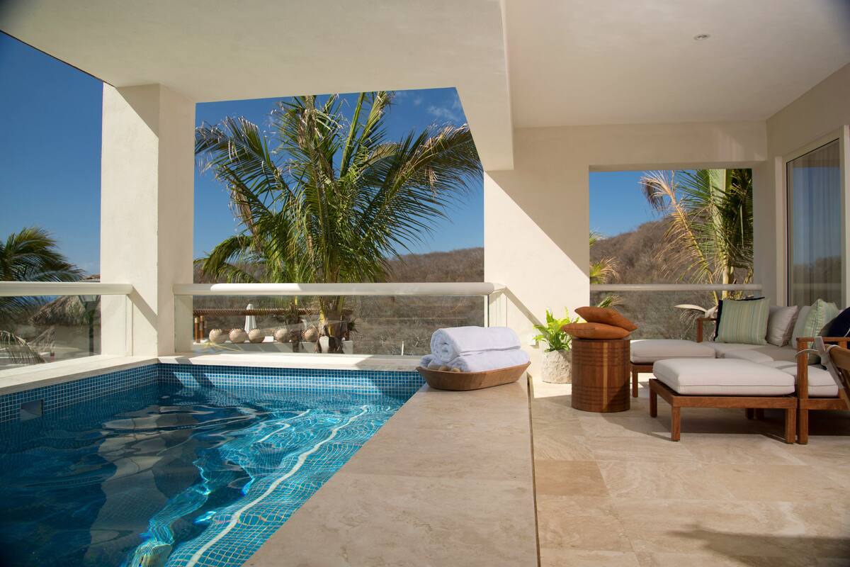 Un área de piscina moderna al aire libre con vistas despejadas a palmeras y una montaña en el fondo.