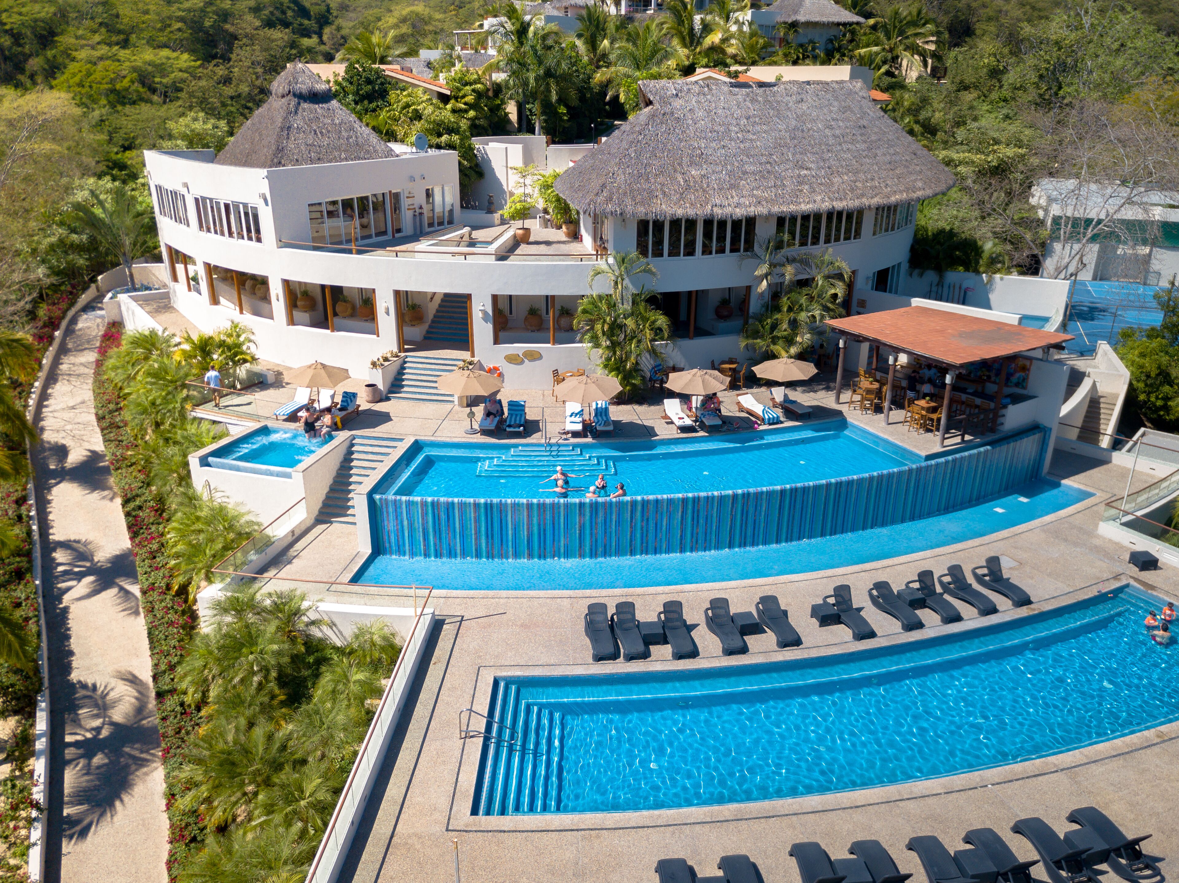 A resort with a large pool, sun loungers, and a bar area.