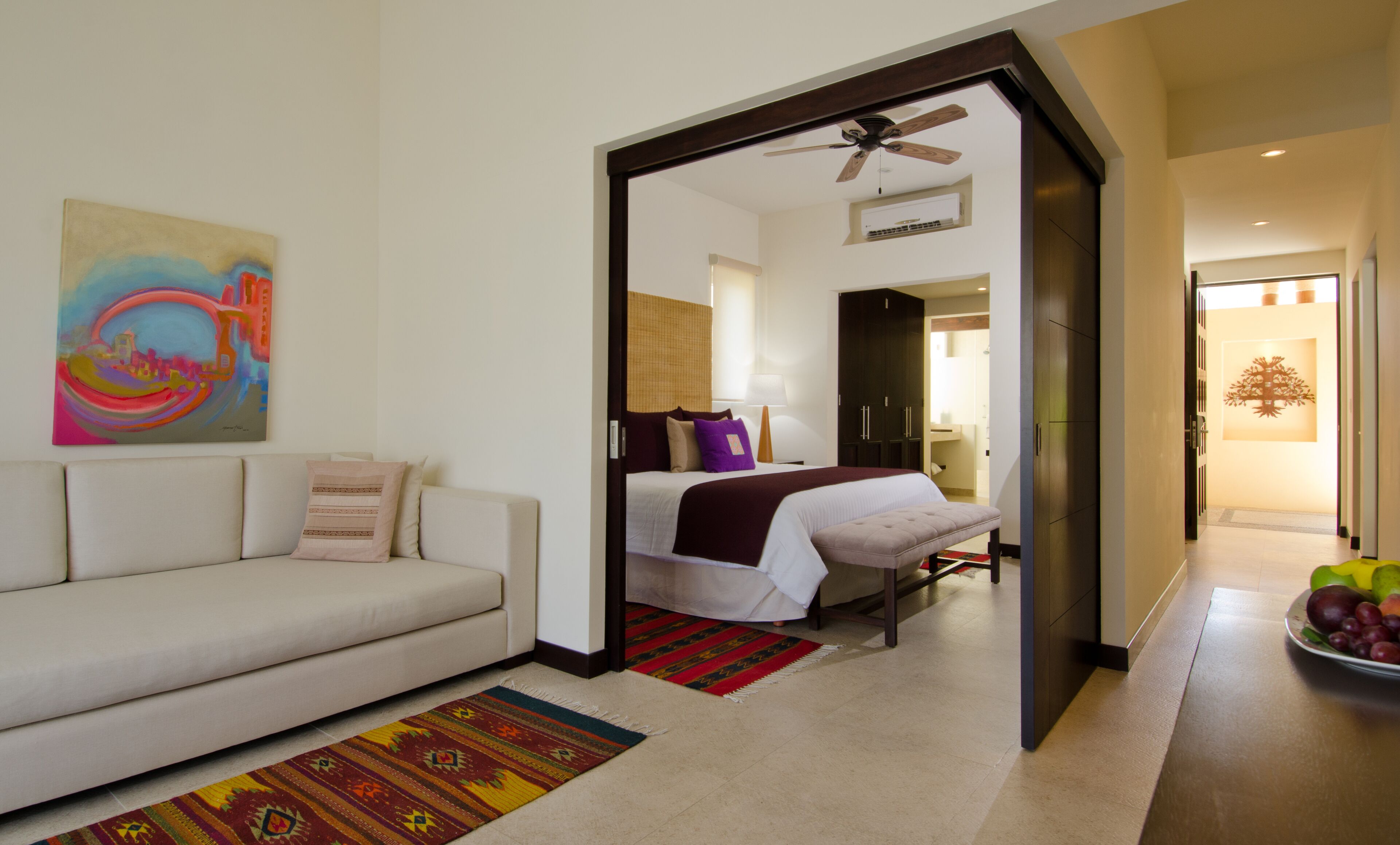 A hotel room with a bed, a sofa, a painting, and a fruit bowl.