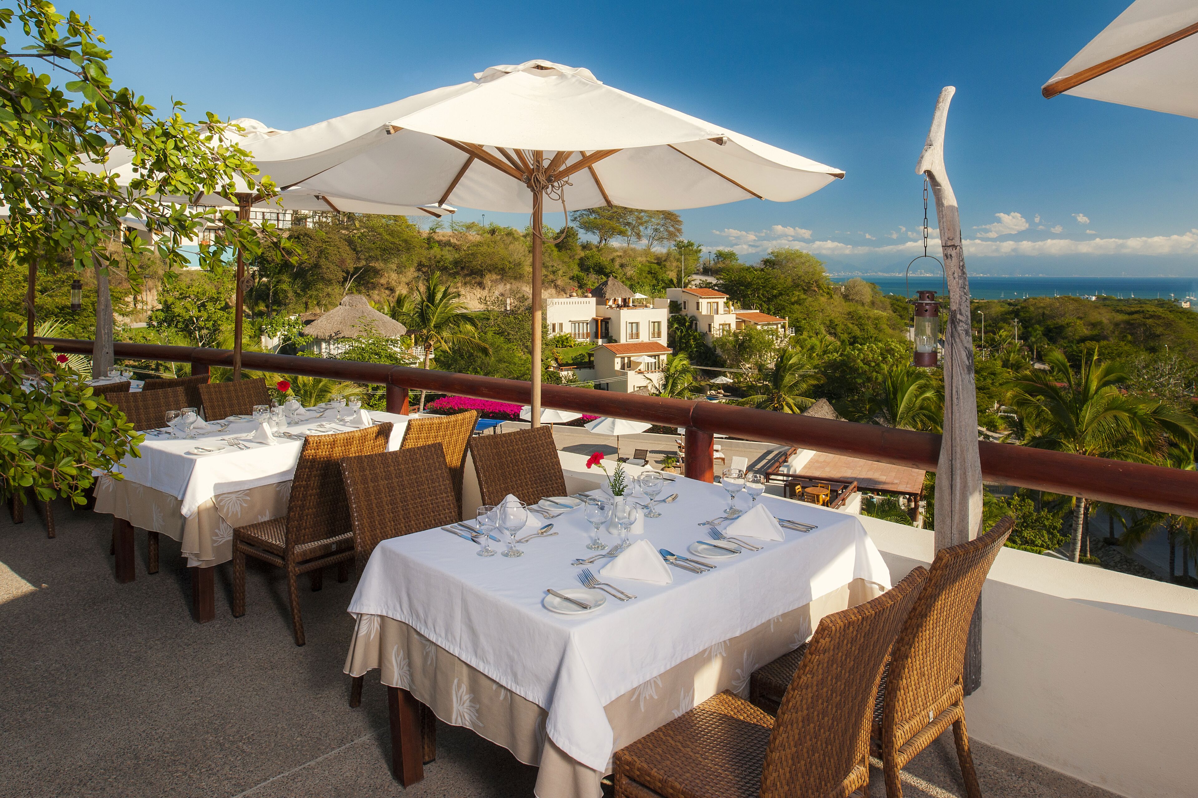 Eine Terrasse mit gedeckten Tischen, mit Blick auf eine reizvolle Landschaft mit Gebäuden und Bäumen.