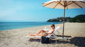 Eine Strandansicht mit einer Person, die unter einem Sonnenschirm entspannt, einem Stuhl und einer Tasche im Sand.