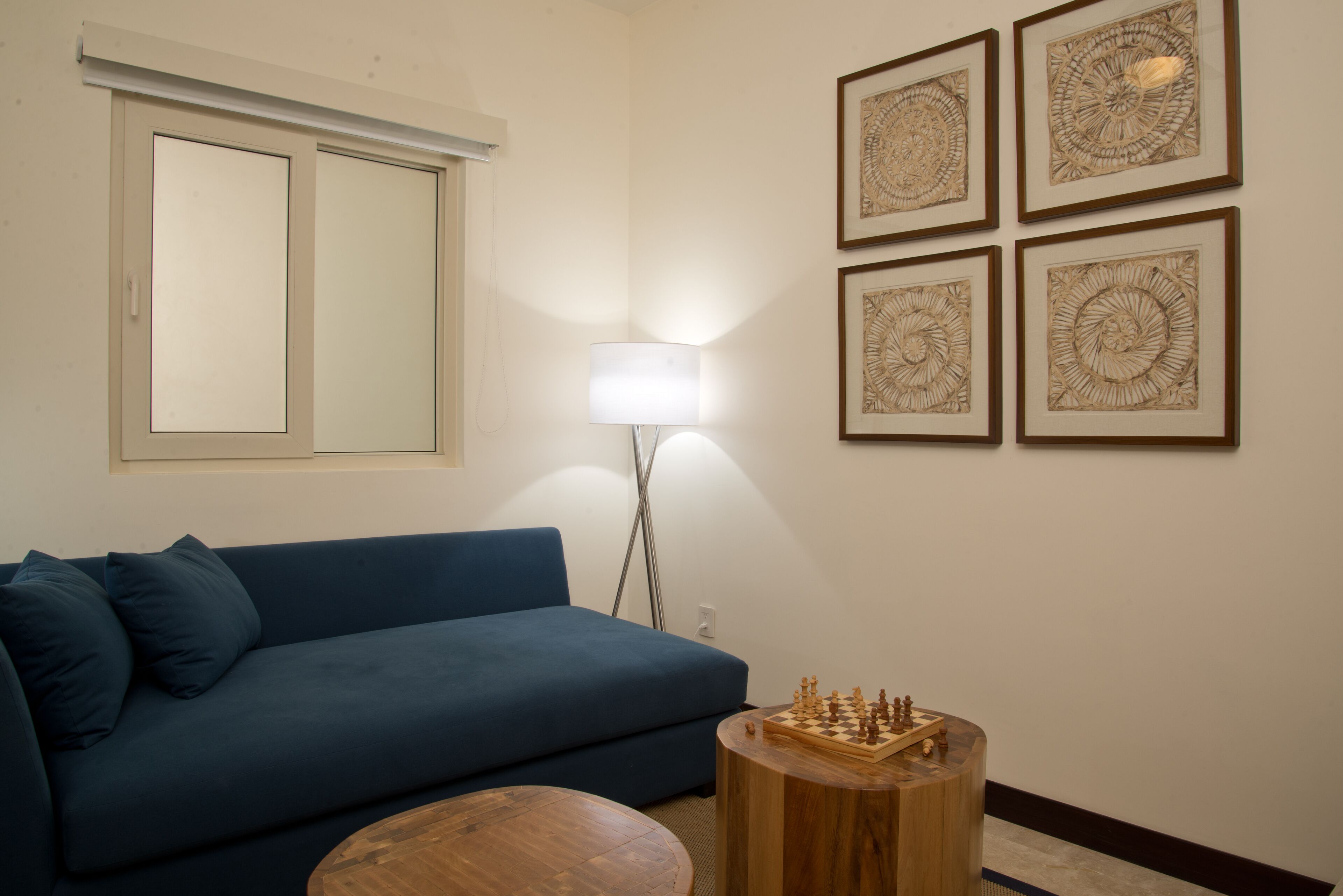 Een woonkamer met een blauwe bank, een ronde houten salontafel en een schaakbord.