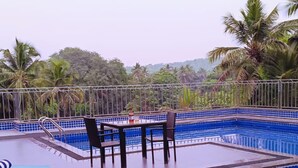 A rooftop pool area with blue tiled edges, lounge chairs, and a table with chairs. - Hotel Meraden Opus (Anjuna)