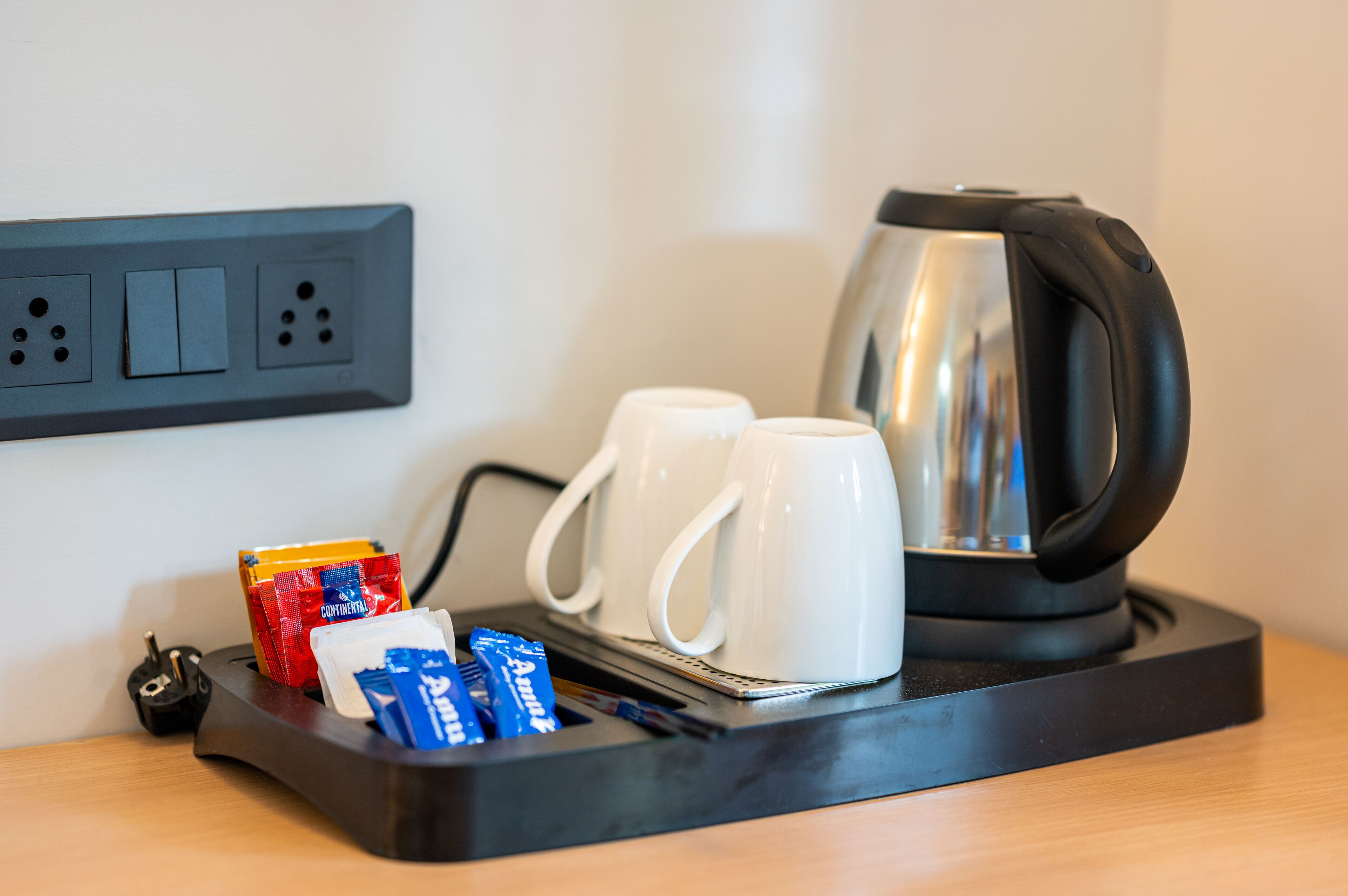 Una estación de café con una tetera, dos tazas blancas y sobres de leche condensada y azúcar.
