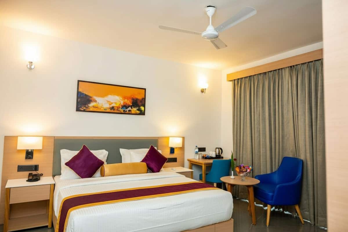 Une chambre d’hôtel avec un lit, un bureau, une chaise, une table, un ventilateur de plafond et un tableau au mur.