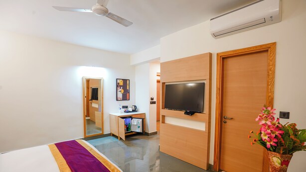 A hotel room with a bed, a desk with a TV, a mirror, and a door. - Hotel Meraden Opus (Anjuna)
