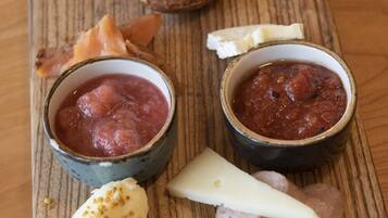 A wooden board with various food items including cheese, sausage, and a bowl of red sauce.