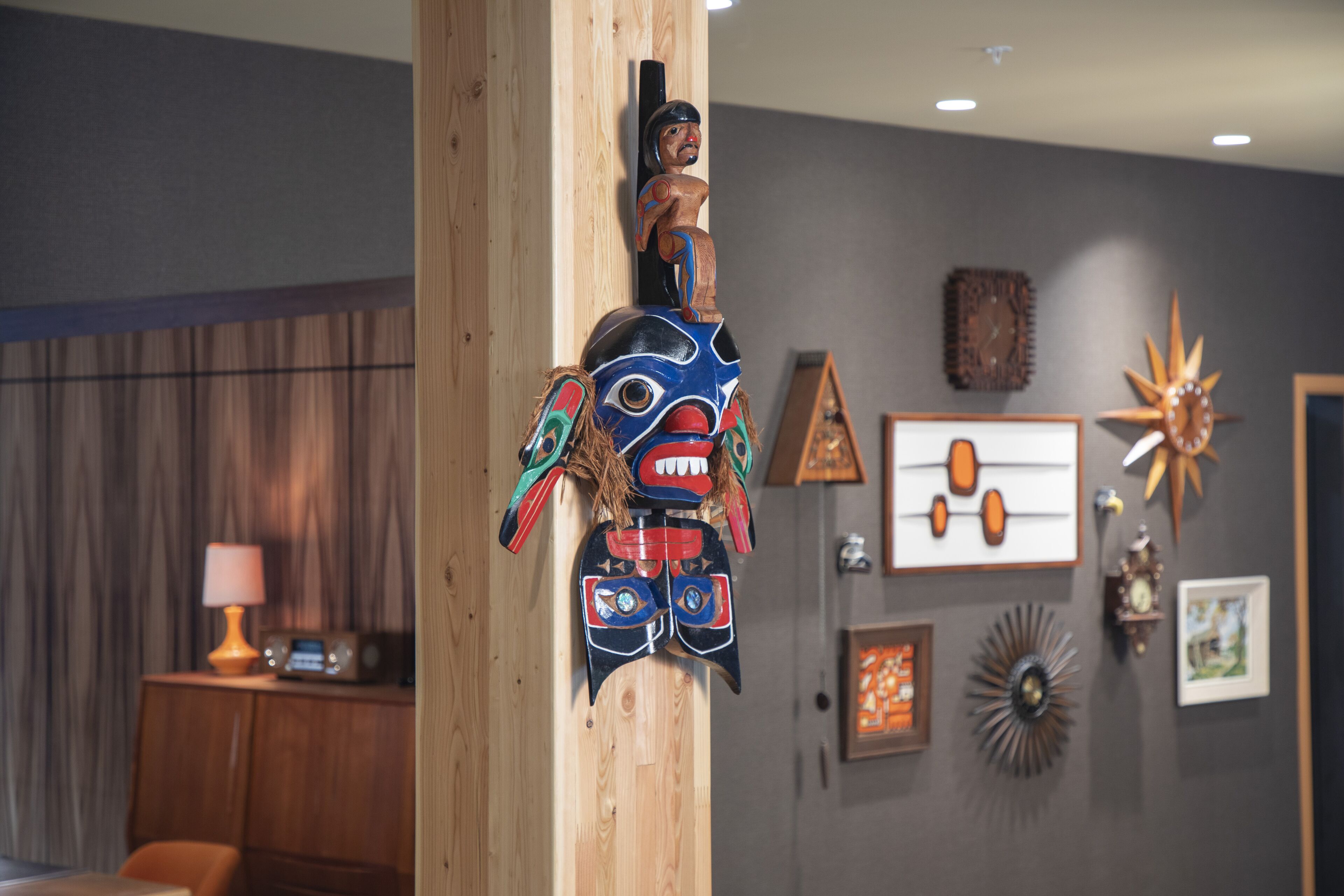 A room with a wooden totem, a lamp, and various wall decorations including a clock and framed pictures.