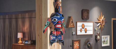 A room with a wooden totem, a lamp, and various wall decorations including a clock and framed pictures.