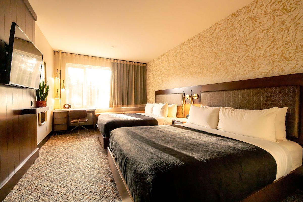 Une chambre d’hôtel avec deux lits, un bureau, une télévision et une fenêtre avec des rideaux.