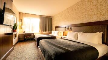 Een hotelkamer met twee bedden, een bureau, een televisie en een raam met gordijnen.