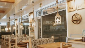 A restaurant with wooden benches and tables, hanging lanterns, and a view of the outside through large windows. - Hotel Zed Tofino (Tofino)
