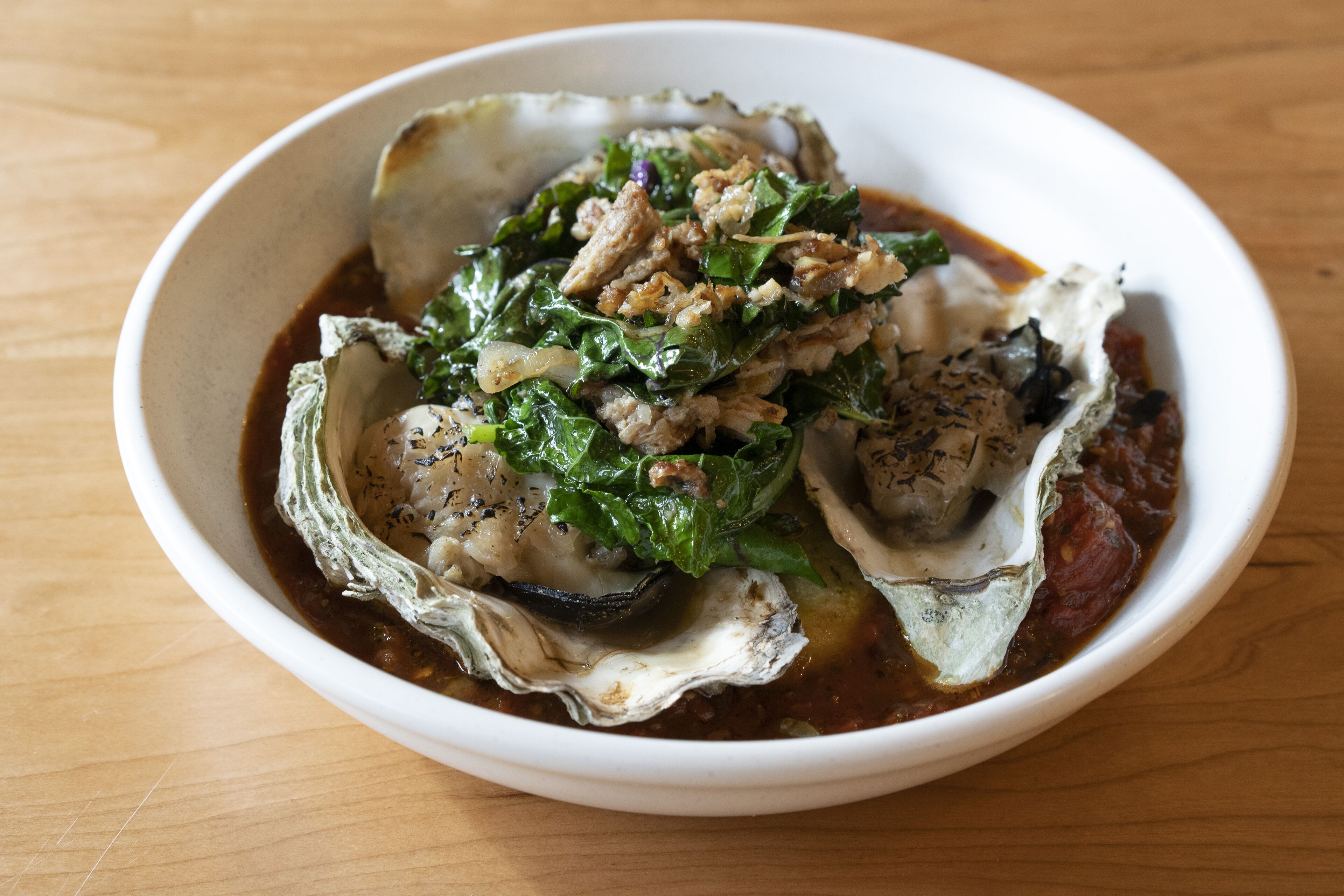 Een schaal met oesters, groenten en vlees op een houten tafel.