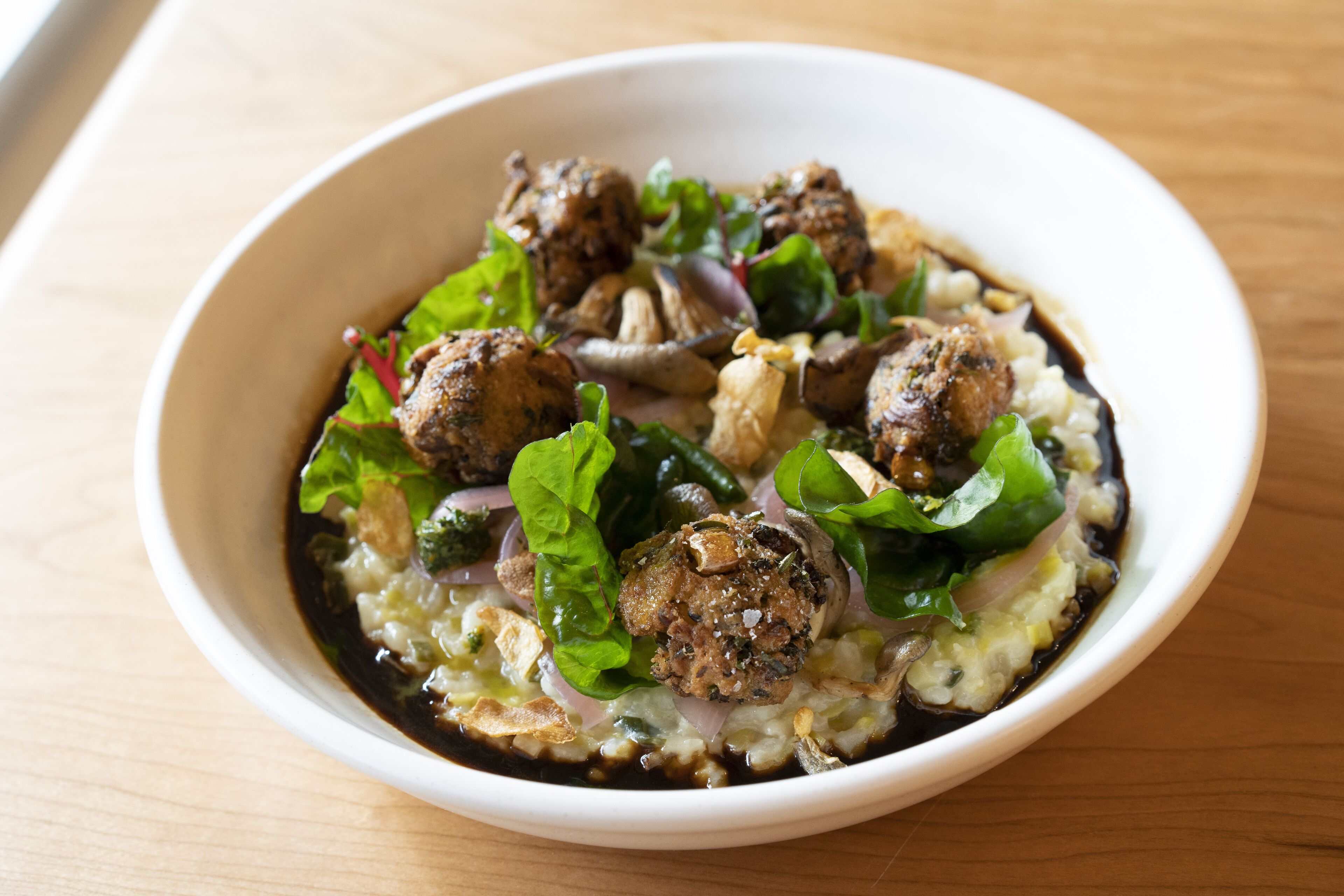 A bowl of food with meatballs, greens, and a creamy base.