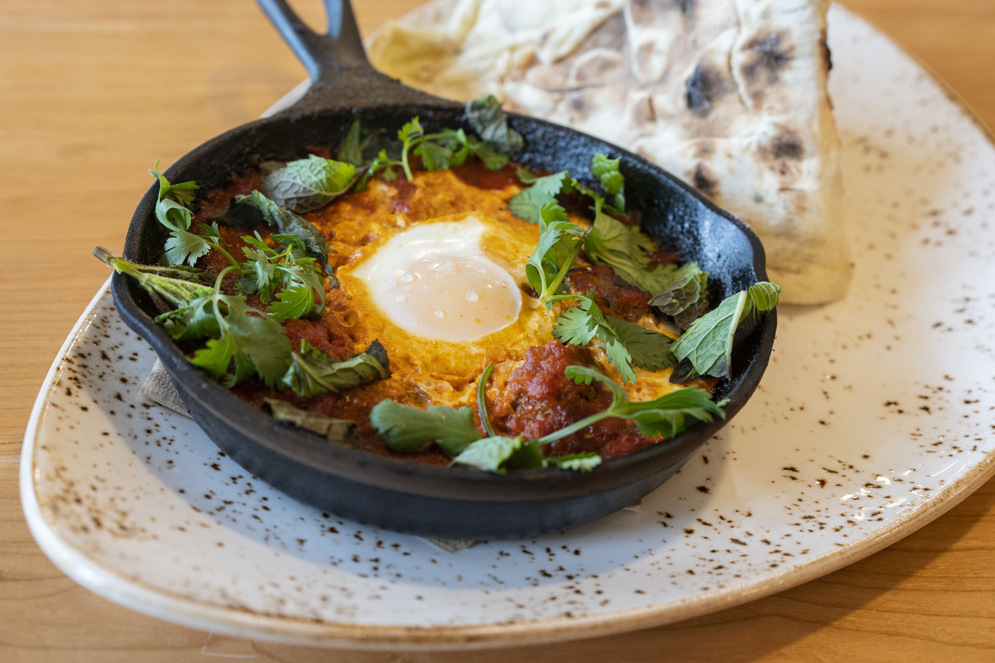 A skillet with a poached egg, garnished with herbs, on a ceramic plate.