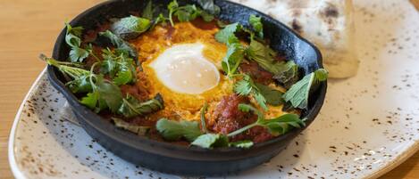 A skillet with a poached egg, garnished with herbs, on a ceramic plate.