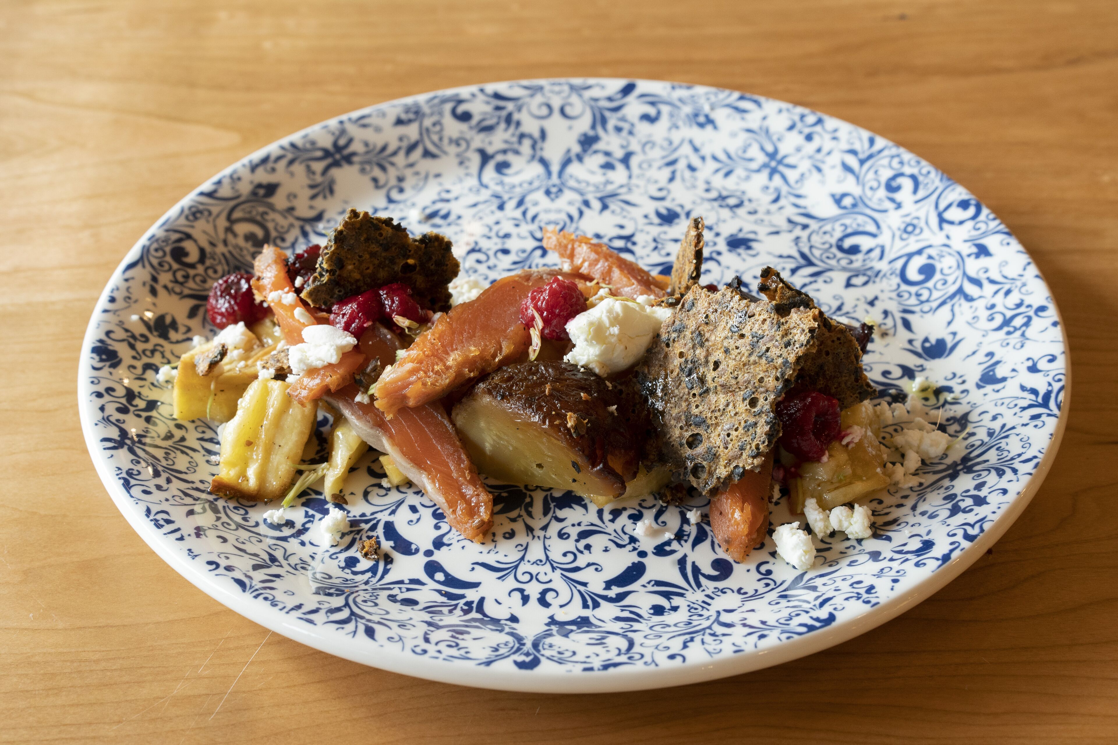 A plate with various food items including salmon, cheese, and crackers on a patterned plate.