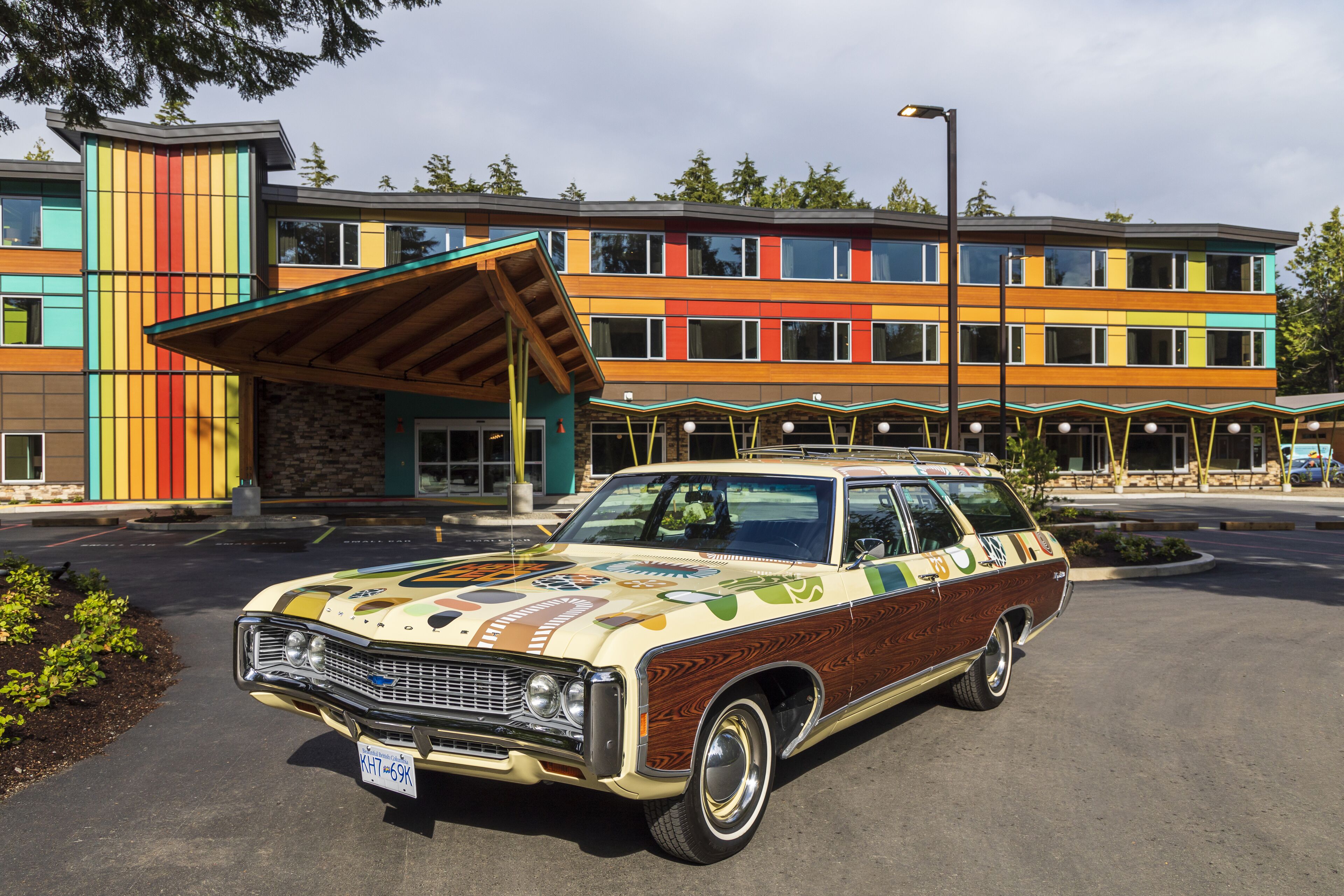 A vintage car parked in front of a colorful building with a modern design.