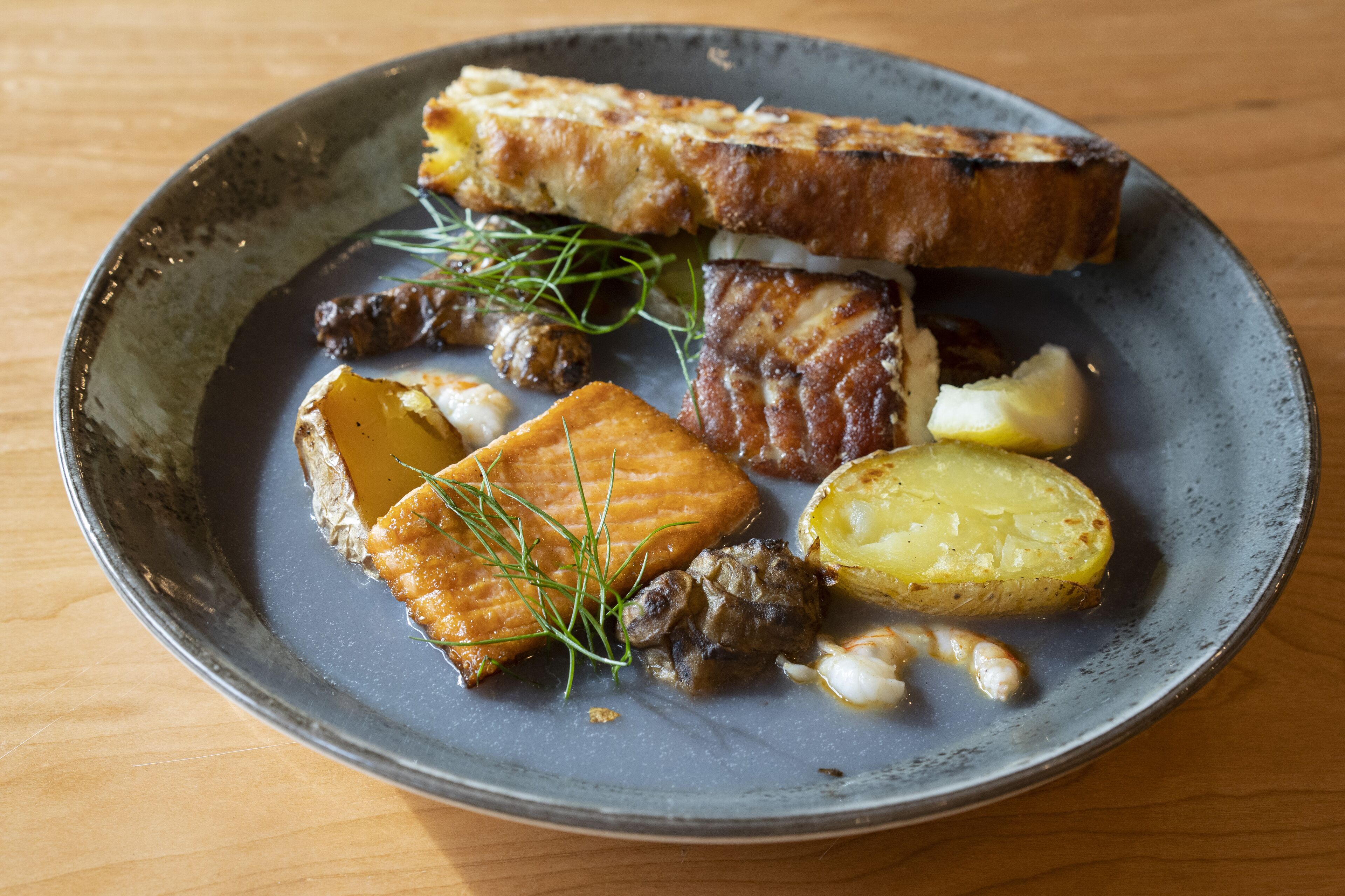 A plate with grilled salmon, potatoes, and a piece of bread on a ceramic plate.