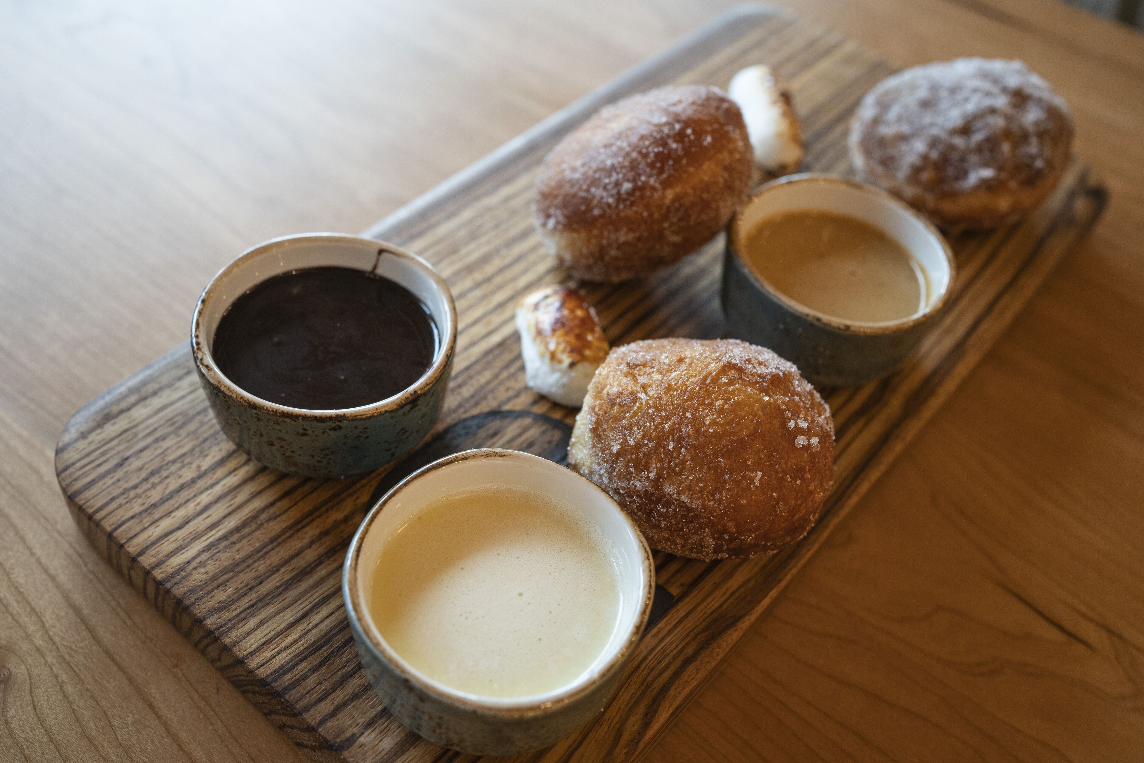 A wooden board with pastries and two cups of coffee on a table.