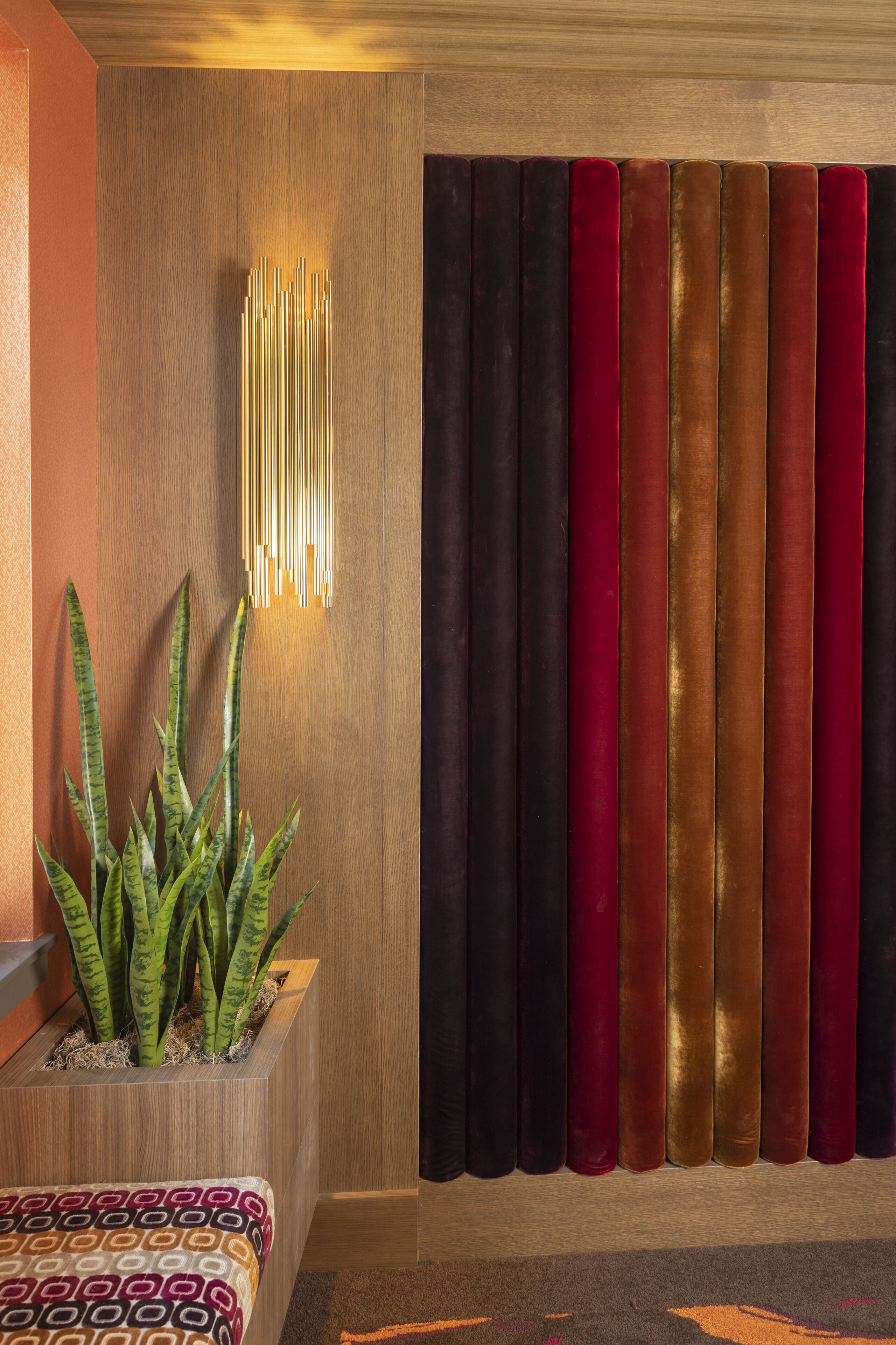 A room with a wooden panel wall, a plant in a wooden planter, and a curtain with vertical stripes in various colors.