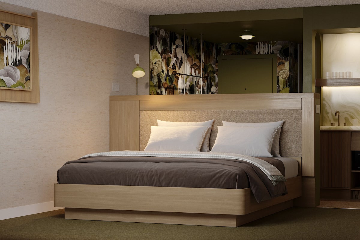 Une chambre à coucher moderne avec un lit en bois, une table de chevet, une lampe fixée au mur et un tableau.