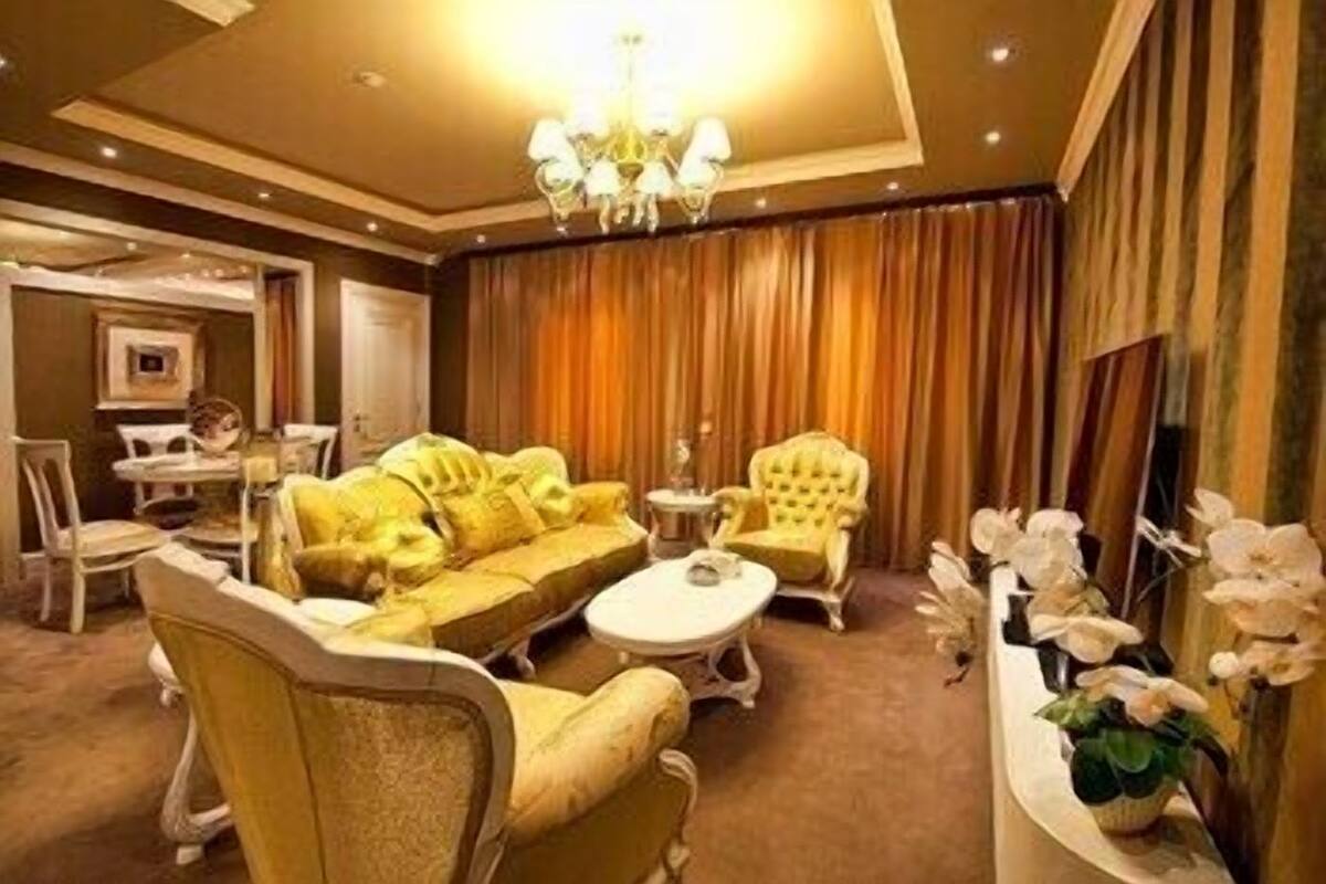 A room with a yellow sofa set, a round coffee table, a yellow armchair, a white side table, and a chandelier.