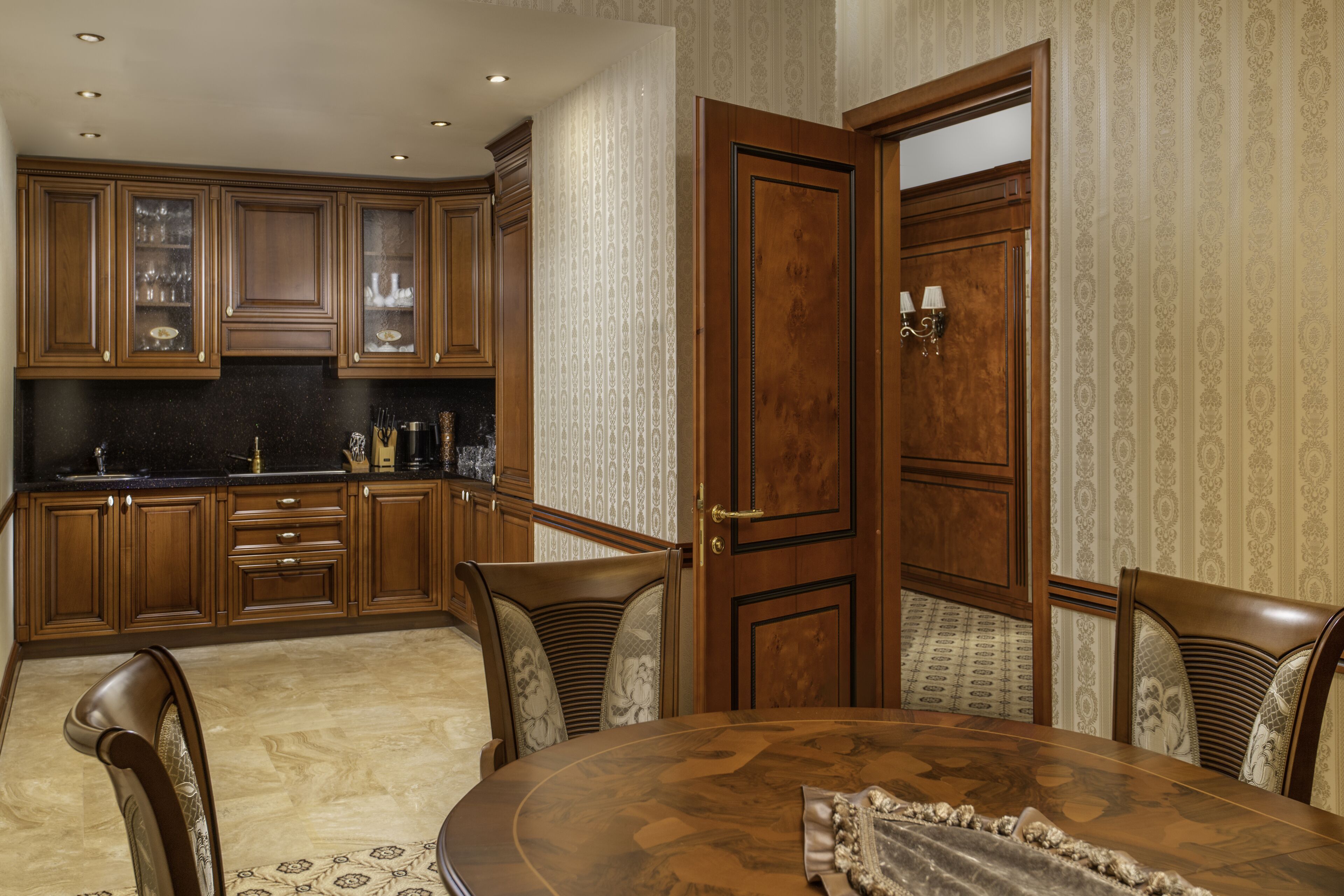 A dining area with a round table and chairs, wooden cabinets, and a patterned wallpaper.