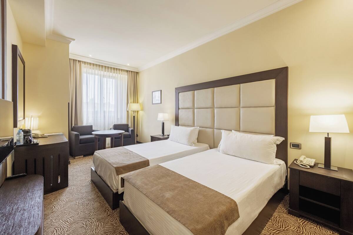 Ein Hotelzimmer mit zwei Betten, einem Schreibtisch, einem Stuhl und einem kleinen Tisch.