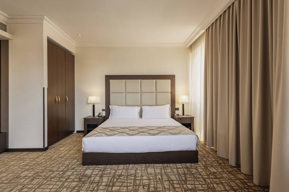 Ein Hotelzimmer mit einem großen Bett, zwei Nachttischen mit Lampen, einem Kleiderschrank und einem gemusterten Teppich.
