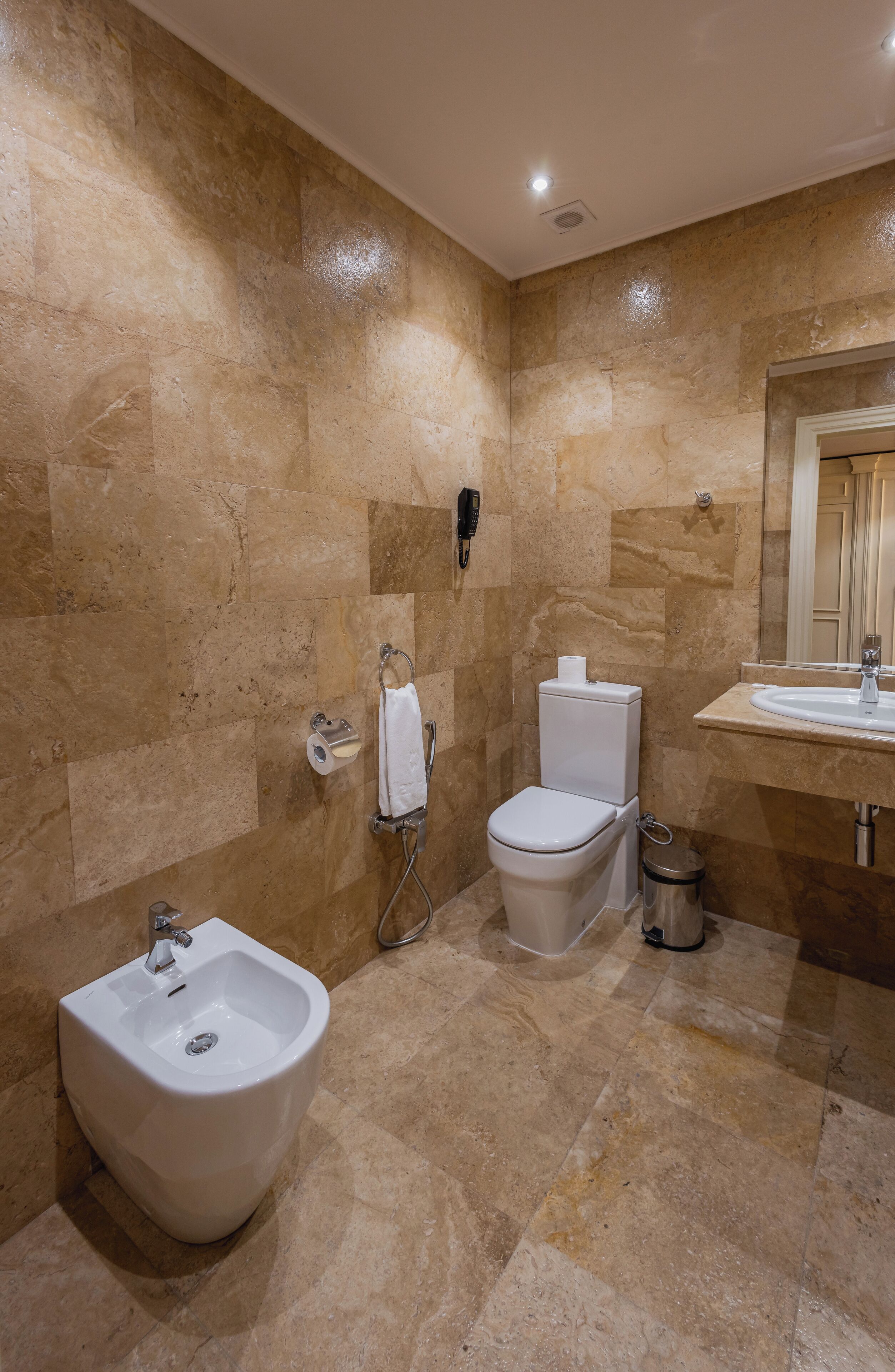 A bathroom with a bidet, toilet, sink, and mirror.
