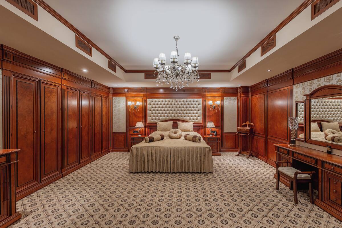 Ein geräumiges Schlafzimmer mit einem großen Bett, Holzvertäfelung, einer Chandelier und einem gemusterten Teppich.