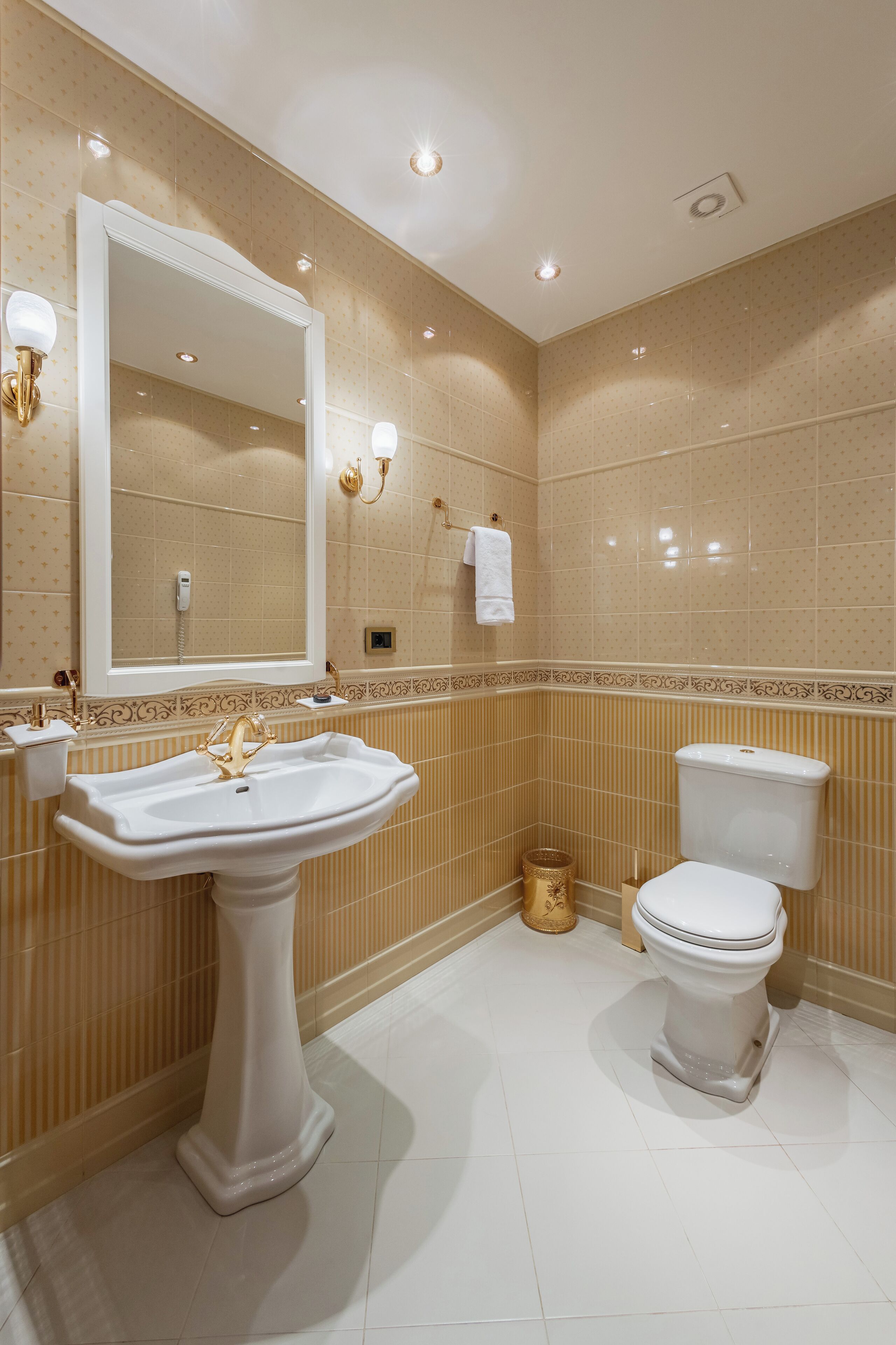 A bathroom with a pedestal sink, a toilet, and a mirror with wall sconces.