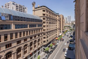 Un edificio de varios pisos con un amplio frente de vidrio y techo curvo, junto a una calle con coches estacionados y aceras.