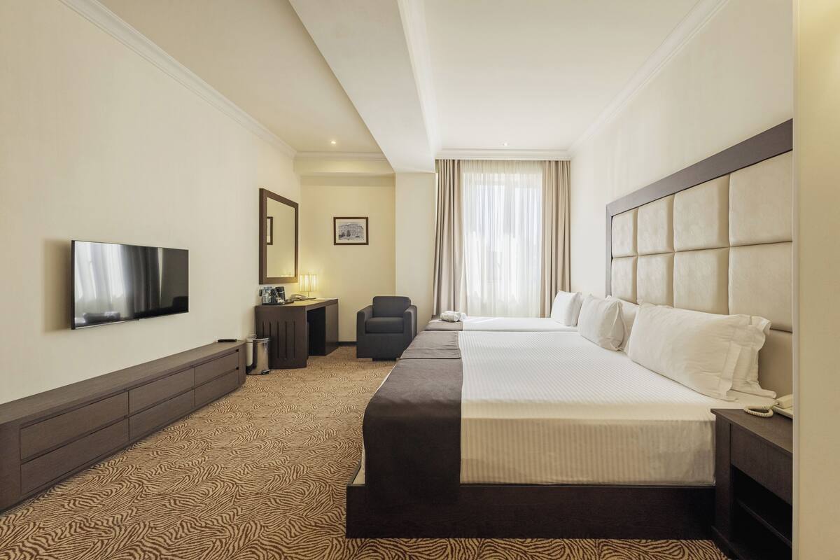 Ein Hotelzimmer mit einem großen Bett, einem Fernseher, einem Schreibtisch und einem Sessel.
