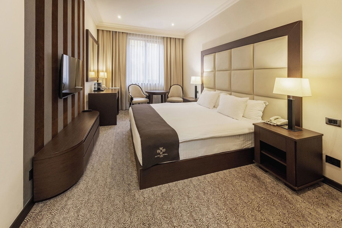 A hotel room with a large bed, a TV, a desk, and a chair.