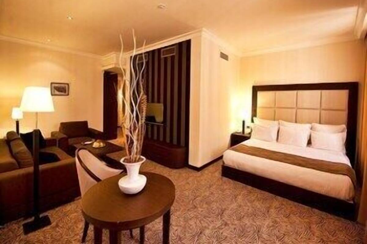 A hotel room with a bed, a sofa, a small table with a vase, and a lamp.