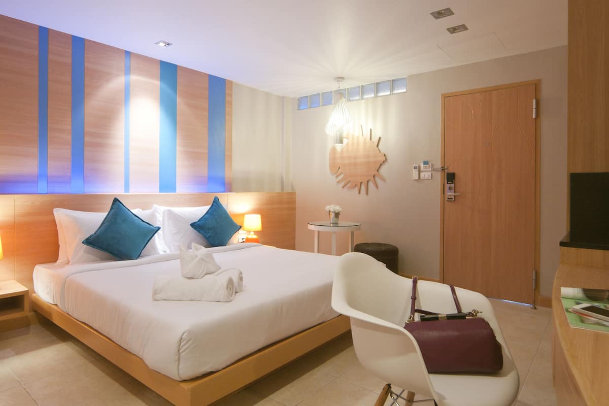 Une chambre d’hôtel moderne avec un grand lit, deux lampes de chevet, une table ronde, une chaise et une porte en bois.