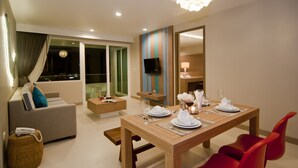Un comedor moderno con una mesa de madera preparada para cuatro personas, un televisor en la pared y un sofá con vista a la ciudad de noche.